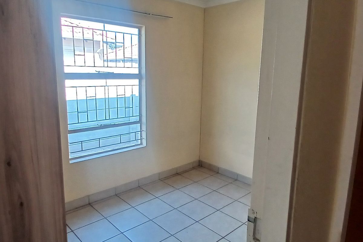 A compact, empty bedroom featuring tiled flooring and a window fitted with security bars.