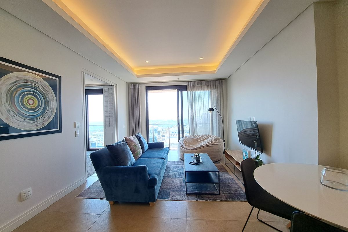 Modern living room featuring recessed cove lighting, large sliding glass doors leading to a balcony, and neutral tiled flooring.