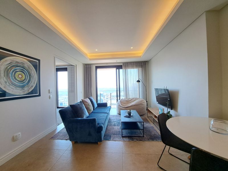 Modern living room featuring recessed cove lighting, large sliding glass doors leading to a balcony, and neutral tiled flooring.