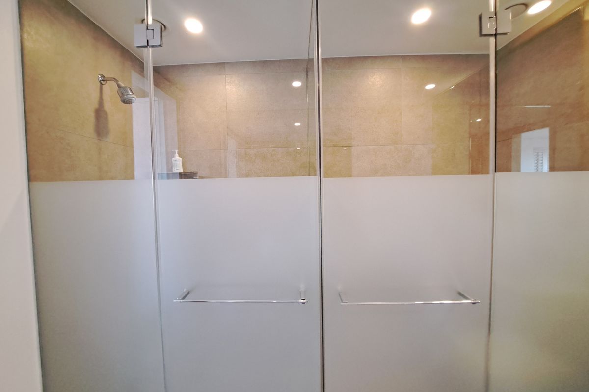 A modern bathroom shower area featuring a glass enclosure with frosted privacy panels and recessed ceiling lighting.