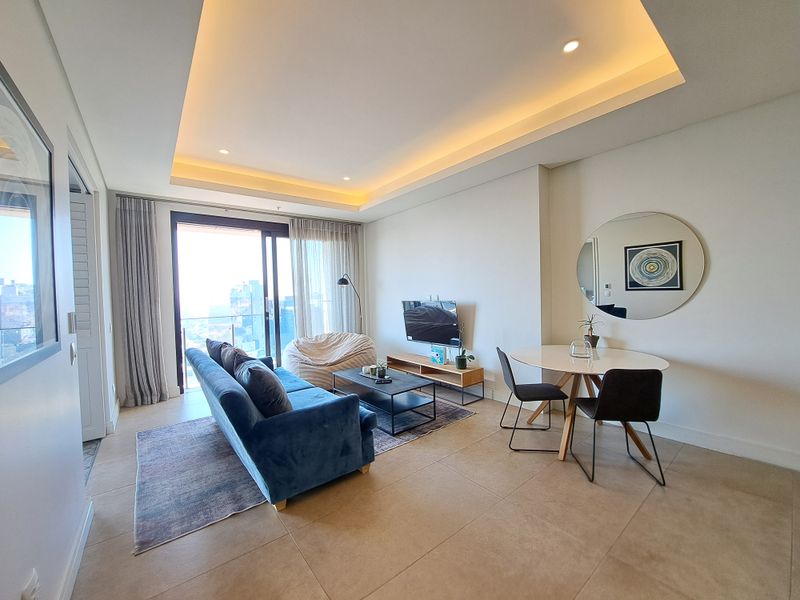 Modern open-plan living and dining area featuring recessed ceiling lighting, large sliding glass doors, and neutral tiled flooring with a bright, airy atmosphere.