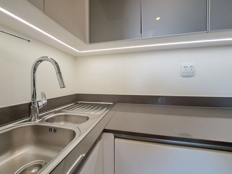 A modern, clean kitchen area featuring a stainless steel sink, chrome mixer tap, integrated cabinetry, and sleek under-cabinet LED lighting.