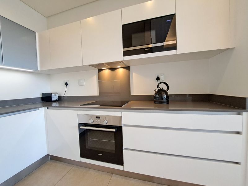 Modern kitchen featuring sleek white cabinetry, stone countertops, integrated Siemens appliances including an oven, hob, and microwave, and a glass splashback.