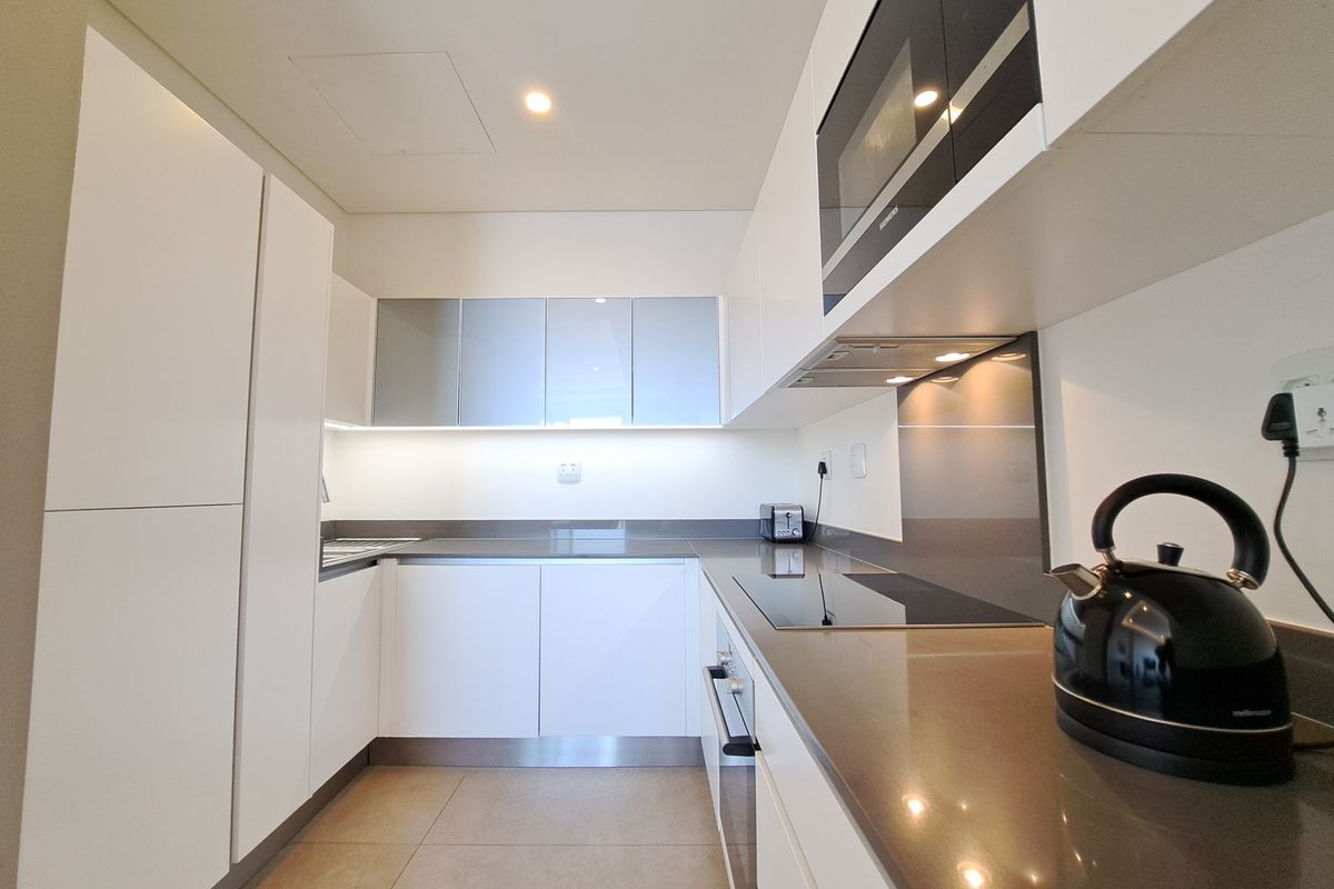 Modern galley-style kitchen featuring sleek white cabinetry, stone countertops, integrated appliances, and high-quality finishes throughout.