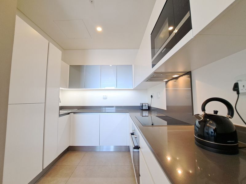 Modern galley-style kitchen featuring sleek white cabinetry, stone countertops, integrated appliances, and high-quality finishes throughout.