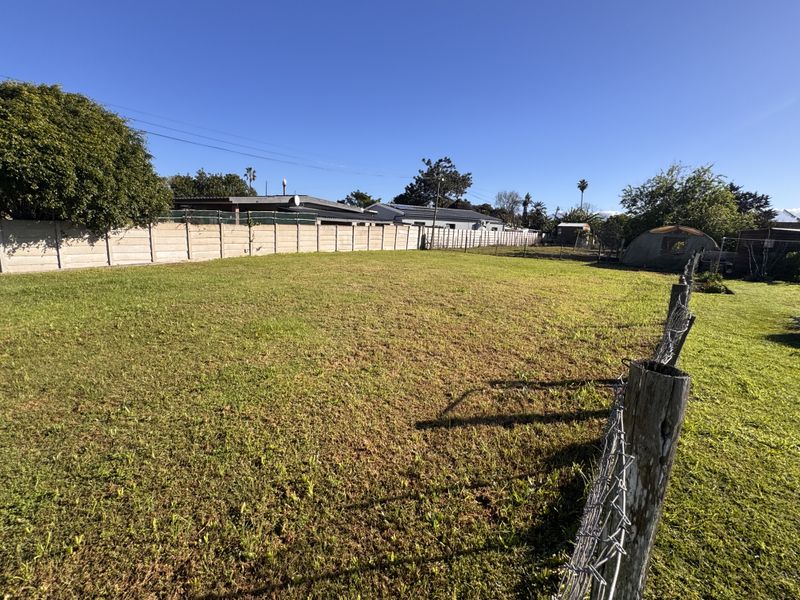 A spacious, open backyard area featuring a large lawn enclosed by precast concrete boundary walls and wire mesh fencing.