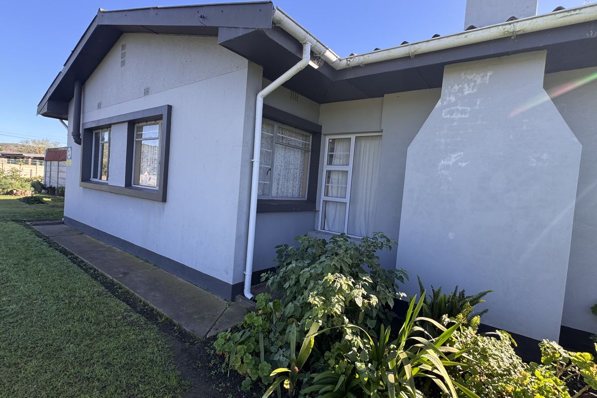 Rear exterior view of the house featuring a concrete pathway, aluminium window frames, and a prominent chimney stack with visible exterior wall weathering.