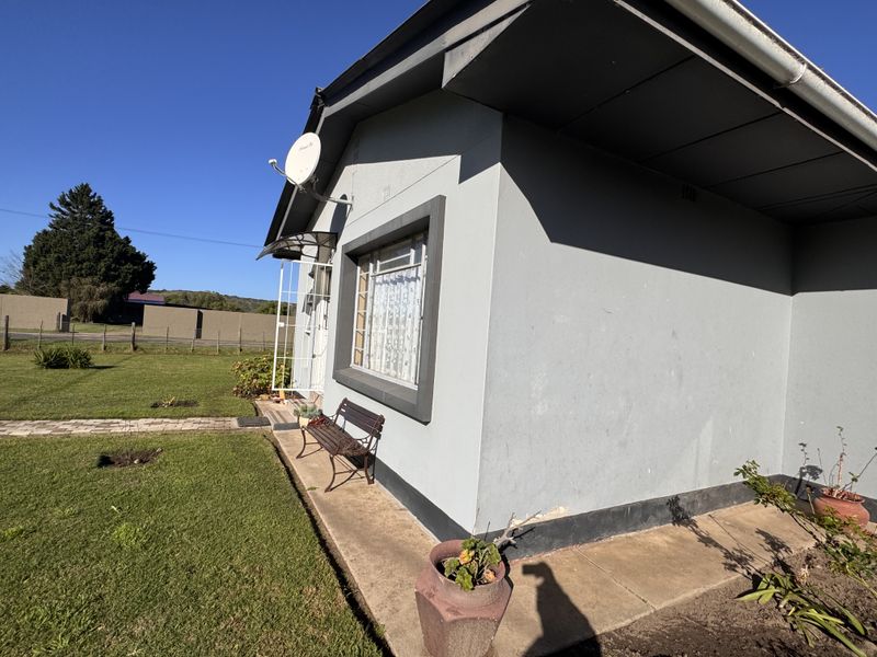 A side view of the property showing the exterior wall, security gate, satellite dish, and surrounding lawn area.