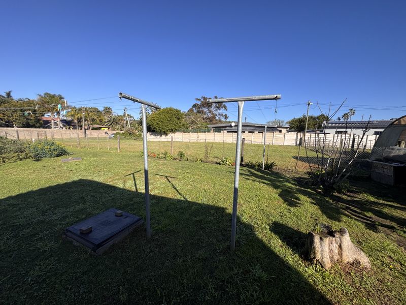 A spacious backyard featuring a lawn, metal washing lines, and a concrete boundary wall.