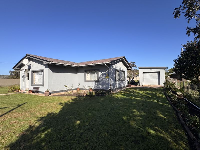Front view of a single-story house featuring a tiled roof, security gates, burglar bars, and a detached garage set on a spacious lawn.