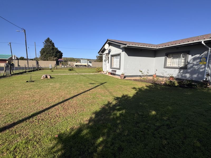 Front view of the house featuring a large lawn, metal roofing, and security window bars, set within a fenced property boundary.
