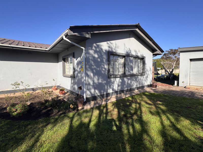 Rear view of the house featuring a metal roof, steel window frames, and an adjacent garage structure set within a garden area.