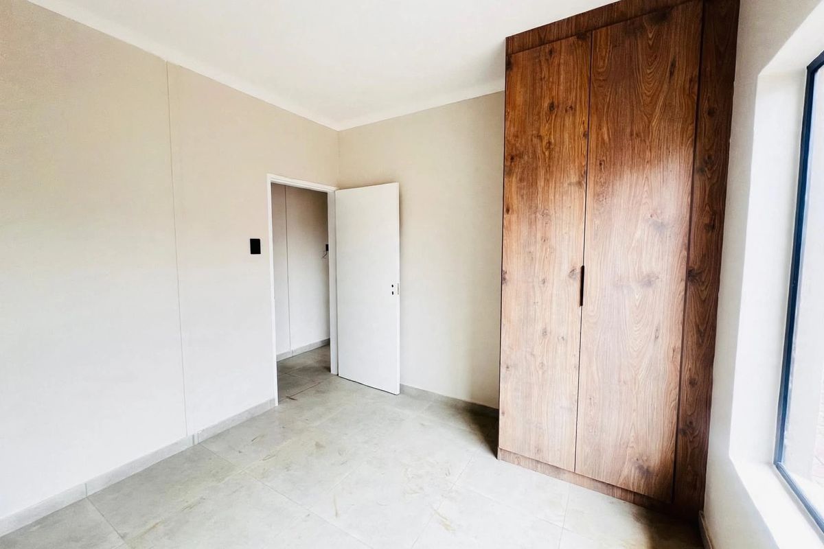 A clean, empty bedroom featuring neutral walls, tiled flooring, and a modern wood-finish built-in wardrobe.