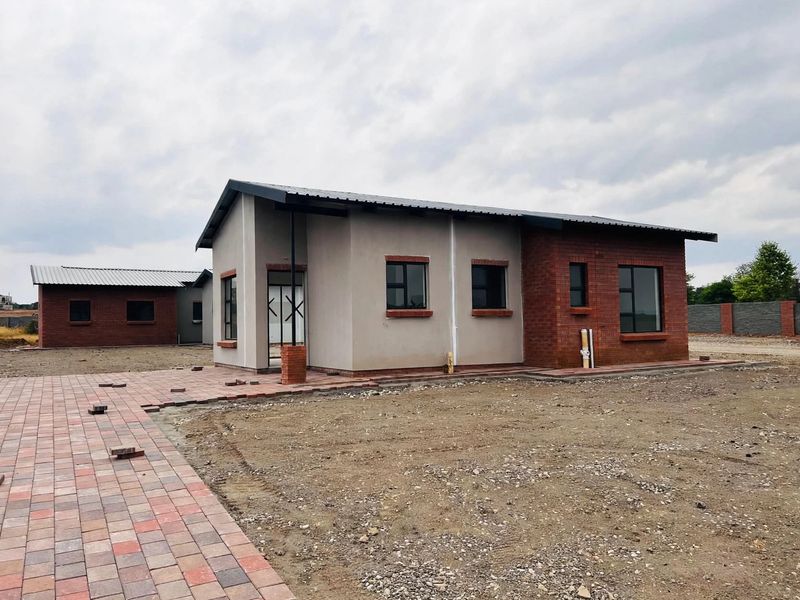 A newly constructed single-story house featuring a combination of brick and plastered exterior walls, metal roofing, and a paved entrance walkway.