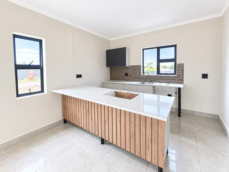 Modern, empty kitchen featuring a central island with a quartz countertop, sleek cabinetry, tiled backsplash, and large windows providing ample natural light.
