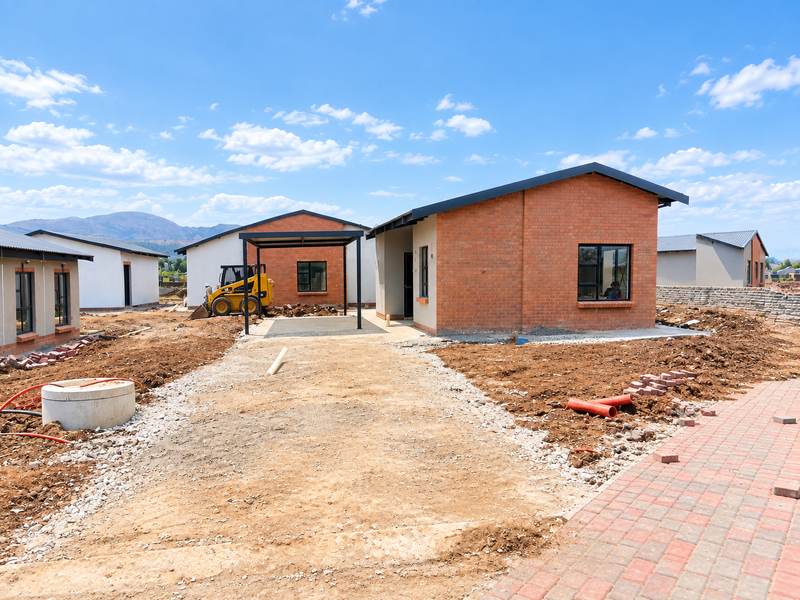 A newly constructed residential development featuring brick houses with metal roofs, carports, and ongoing site landscaping work.