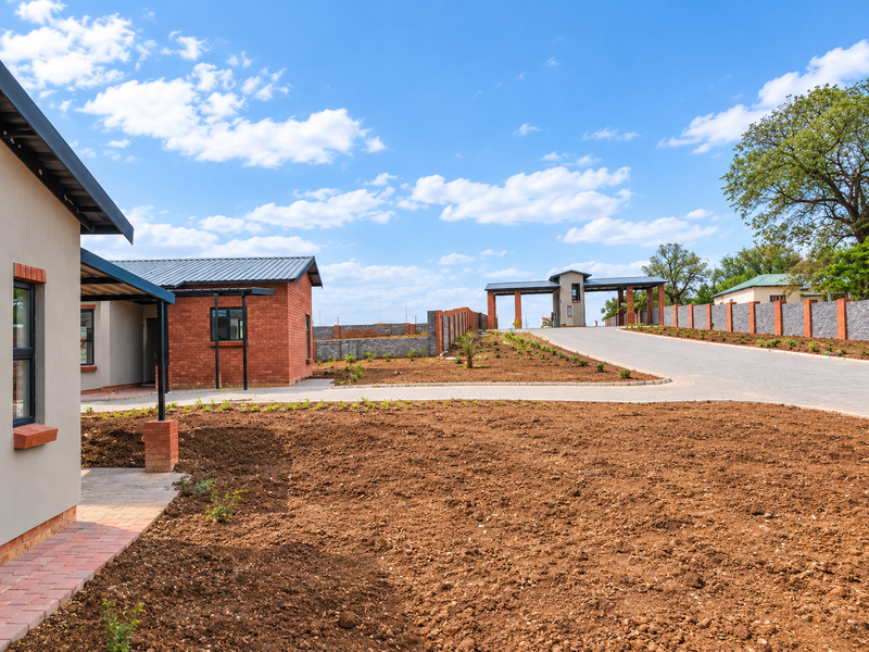 A view of a modern residential complex featuring brick-clad homes, a paved driveway, and a secure gated entrance with an unlandscaped garden area.