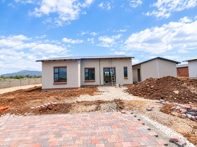 Rear view of a modern single-story house under construction, featuring a metal roof, aluminium windows, and partially completed paved driveway and landscaping.