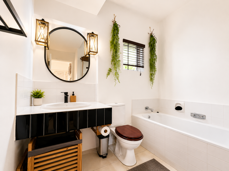 A well-maintained bathroom featuring a modern vanity with a black faucet, a round mirror, a bathtub, and neutral wall tiling.