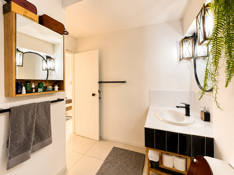 A well-maintained bathroom featuring a tiled vanity with a modern black mixer tap, wall-mounted mirror, and neutral floor tiling.