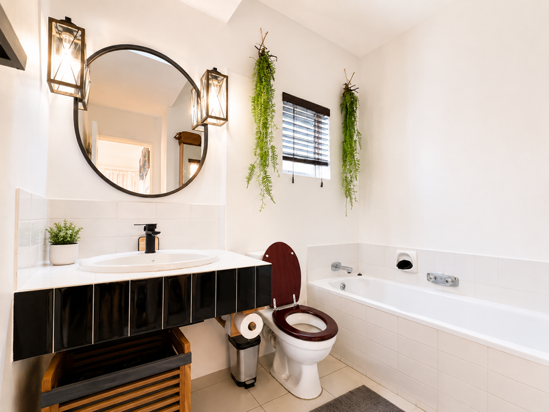 A well-maintained bathroom featuring a vanity basin, bathtub, and modern wall lighting, finished with clean white tiling and a circular mirror.