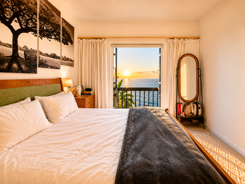 A well-maintained bedroom featuring a balcony door that opens to a scenic ocean sunset view.