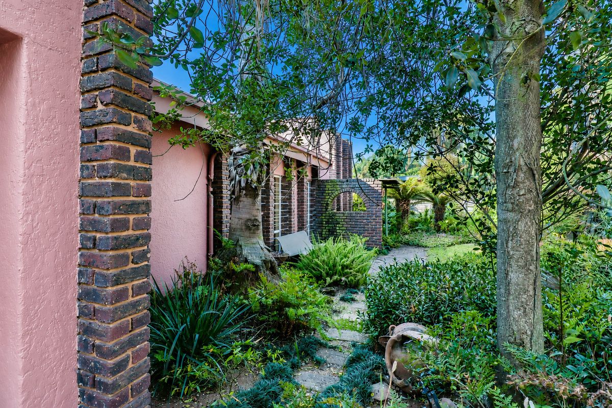A view of the rear exterior featuring brick pillars, a paved garden pathway, and established landscaping.
