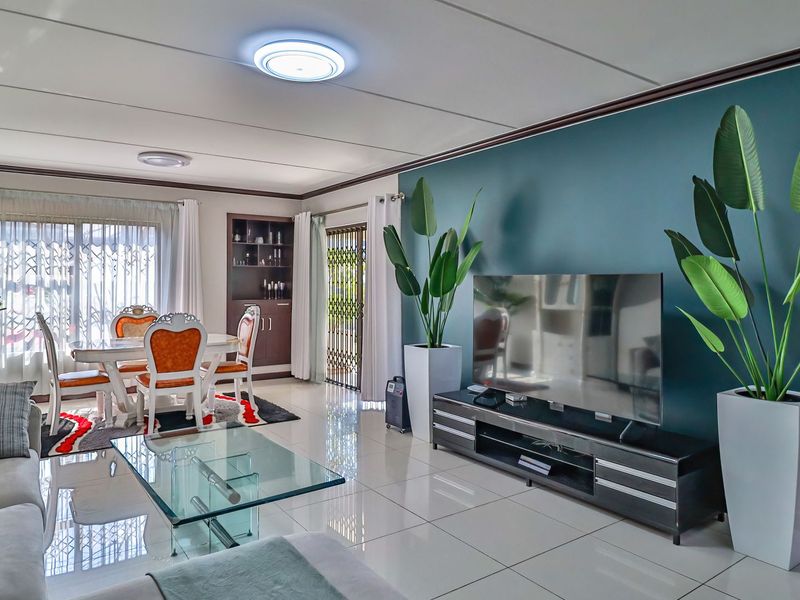 Spacious open-plan living and dining area featuring polished tile flooring, a feature accent wall, and built-in cabinetry with direct access to the exterior.