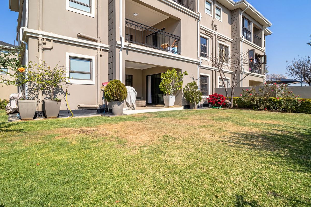 Rear view of the apartment building featuring a private garden, paved patio area, and a balcony with wrought iron railings.