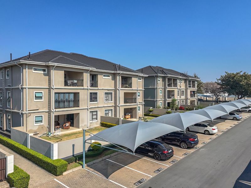 Exterior view of a modern apartment complex featuring multi-story units with balconies, paved parking areas, and shade cloth carports.