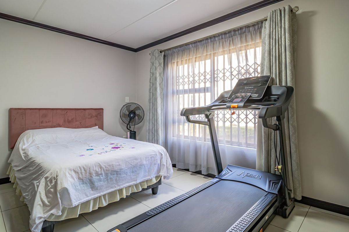 A well-maintained bedroom featuring tiled flooring, crown molding, and a large window fitted with a security gate and curtain rails.