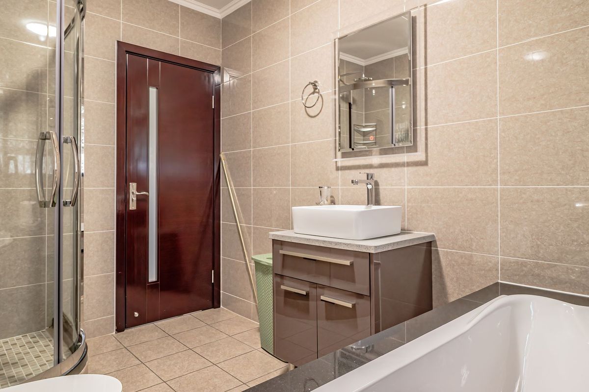 Modern bathroom featuring a glass shower enclosure, a sleek vanity with a vessel sink, a bathtub, and neutral wall tiling.