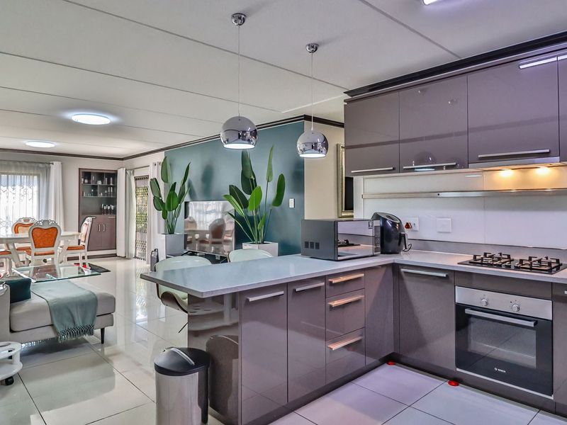 Modern open-plan living area featuring a sleek kitchen with high-gloss cabinetry, integrated appliances, and tiled flooring, seamlessly flowing into the dining and lounge space.