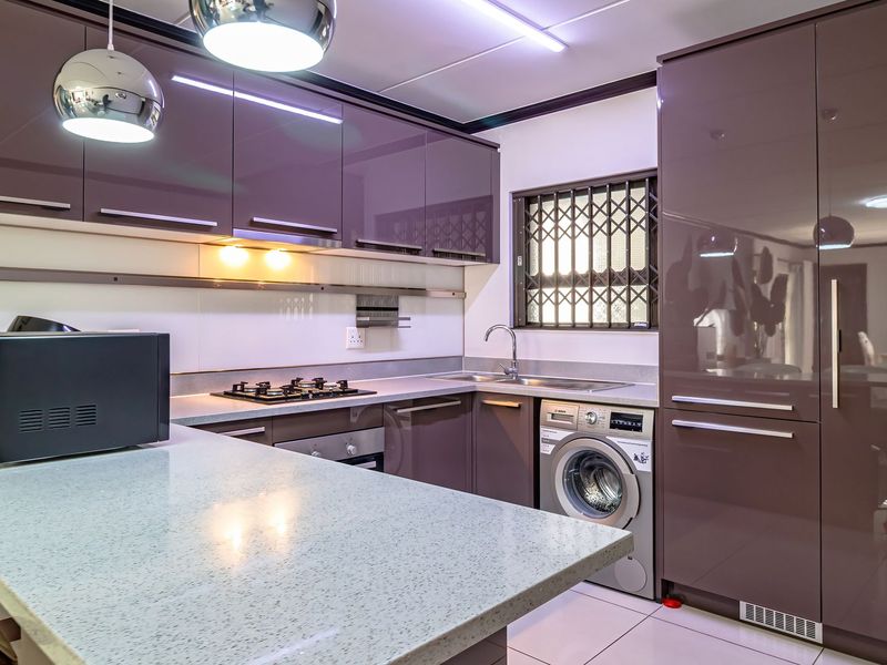 Modern kitchen featuring high-gloss cabinetry, stone countertops, integrated appliances, a gas hob, and a built-in oven with a functional layout.