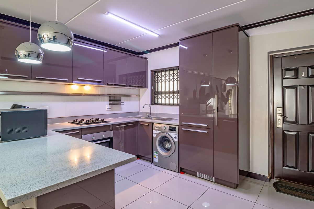 Modern kitchen featuring high-gloss cabinetry, stone countertops, built-in gas hob and oven, integrated washing machine, and tiled flooring with direct access to the entrance.