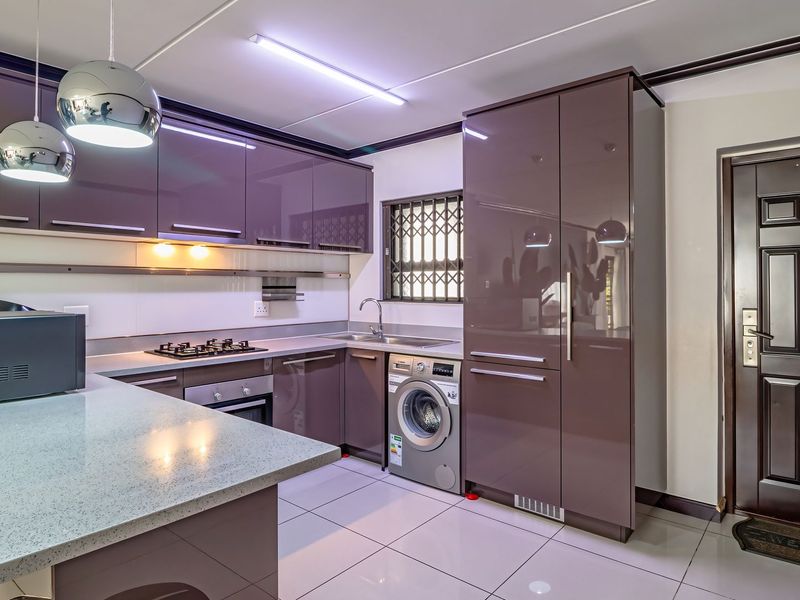 Modern kitchen featuring high-gloss cabinetry, stone countertops, built-in gas hob and oven, integrated washing machine, and tiled flooring with direct access to the entrance.