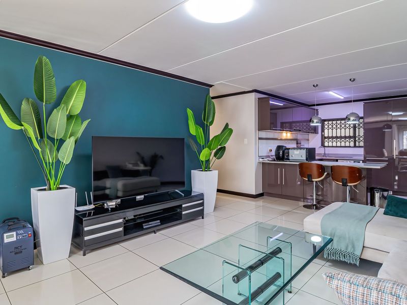 Modern open-plan living area featuring tiled floors, a vibrant accent wall, and a sleek, well-appointed kitchen with a breakfast bar.