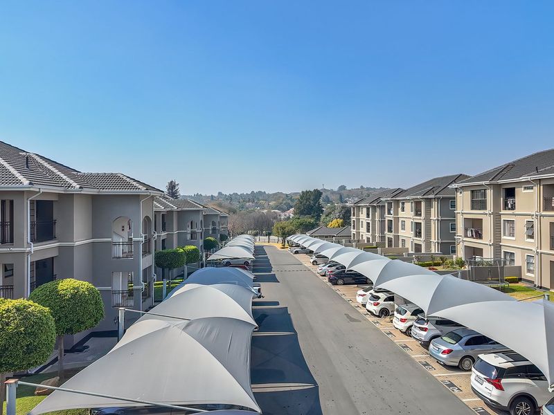 Elevated view of a residential apartment complex featuring multiple multi-story buildings, paved driveway, and covered parking bays with shade cloth structures.