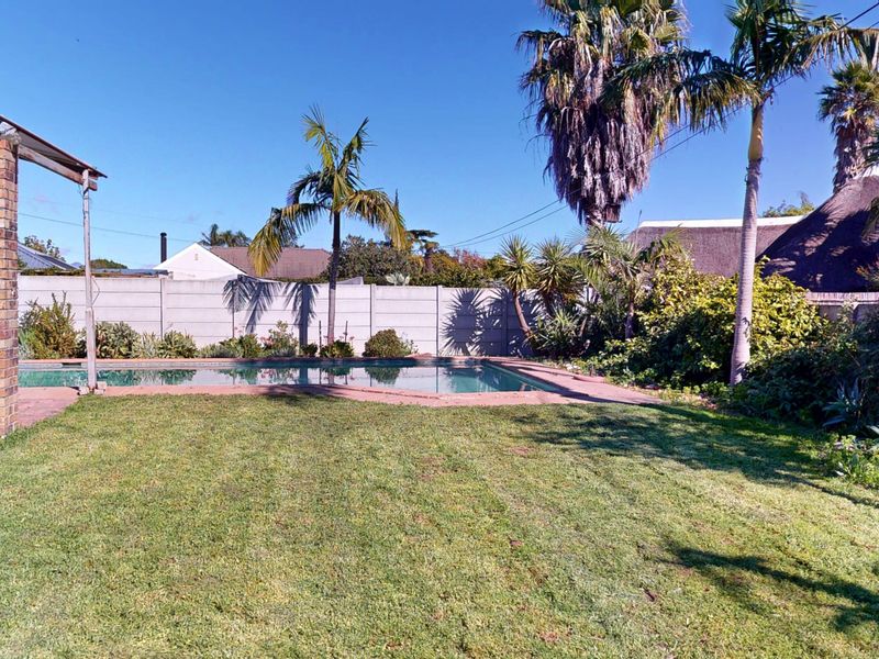 A private backyard featuring a swimming pool, paved surround, and established garden with palm trees, enclosed by a perimeter wall.