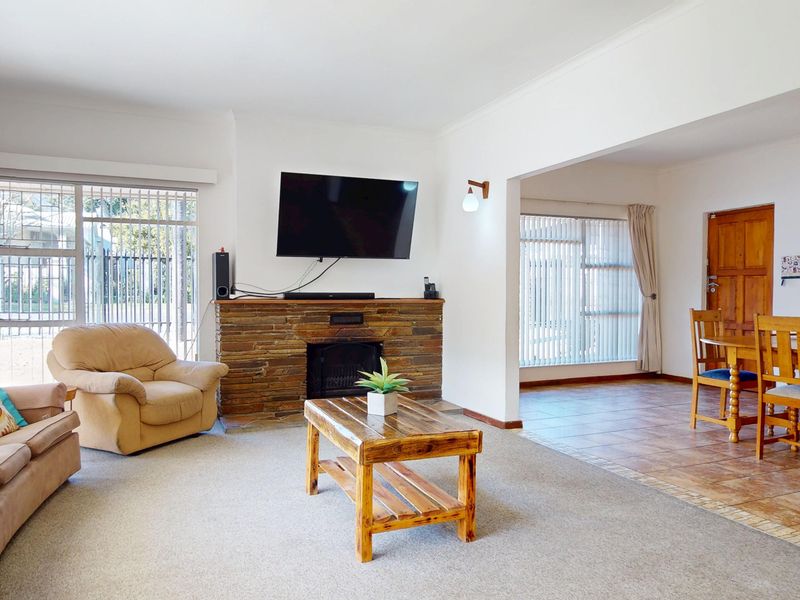 Spacious open-plan living and dining area featuring a stone fireplace, tiled and carpeted flooring, and large windows with security bars.