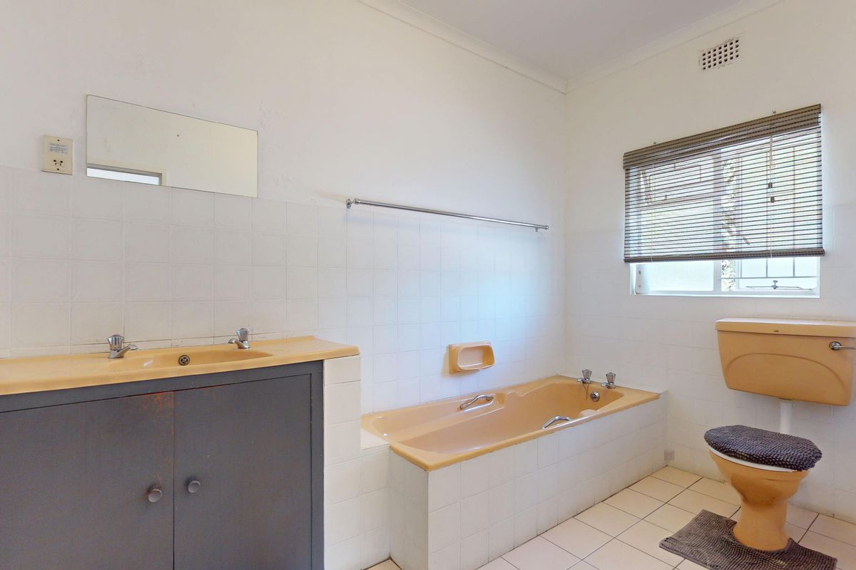 A functional bathroom featuring a built-in vanity, bathtub, and toilet with classic tiled finishes, offering potential for a modern renovation.