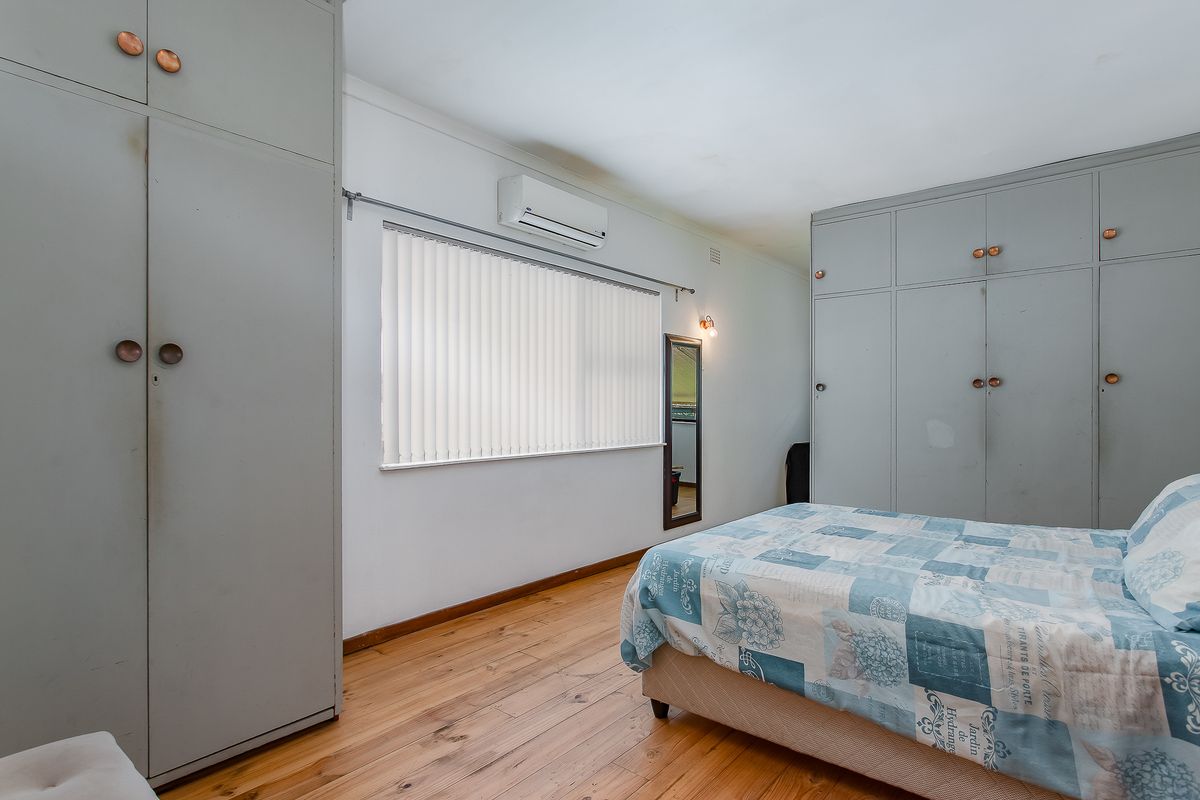 A bedroom featuring timber flooring, built-in cupboards, and a wall-mounted split-system air conditioner.