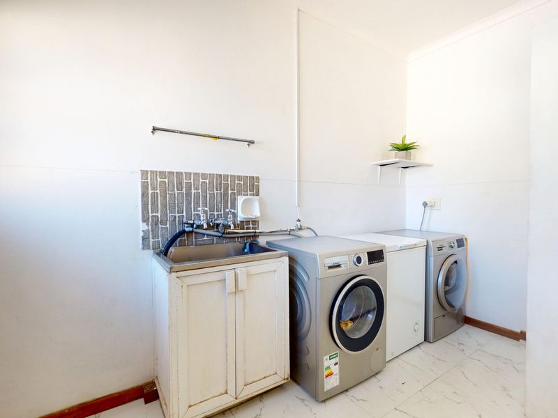 A functional laundry area featuring a stainless steel sink, tiled splashback, and dedicated plumbing connections for laundry appliances.
