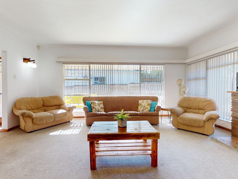 Spacious living room featuring a natural stone fireplace, large windows with vertical blinds, and neutral carpeting.