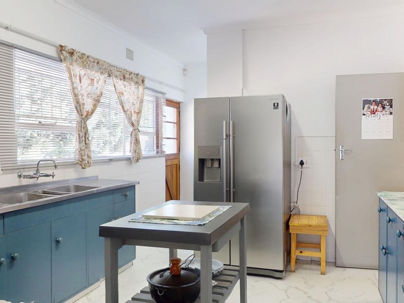 A functional kitchen featuring blue cabinetry, stainless steel double sink, tiled splashbacks, and laminate countertops with a bright, clean layout.