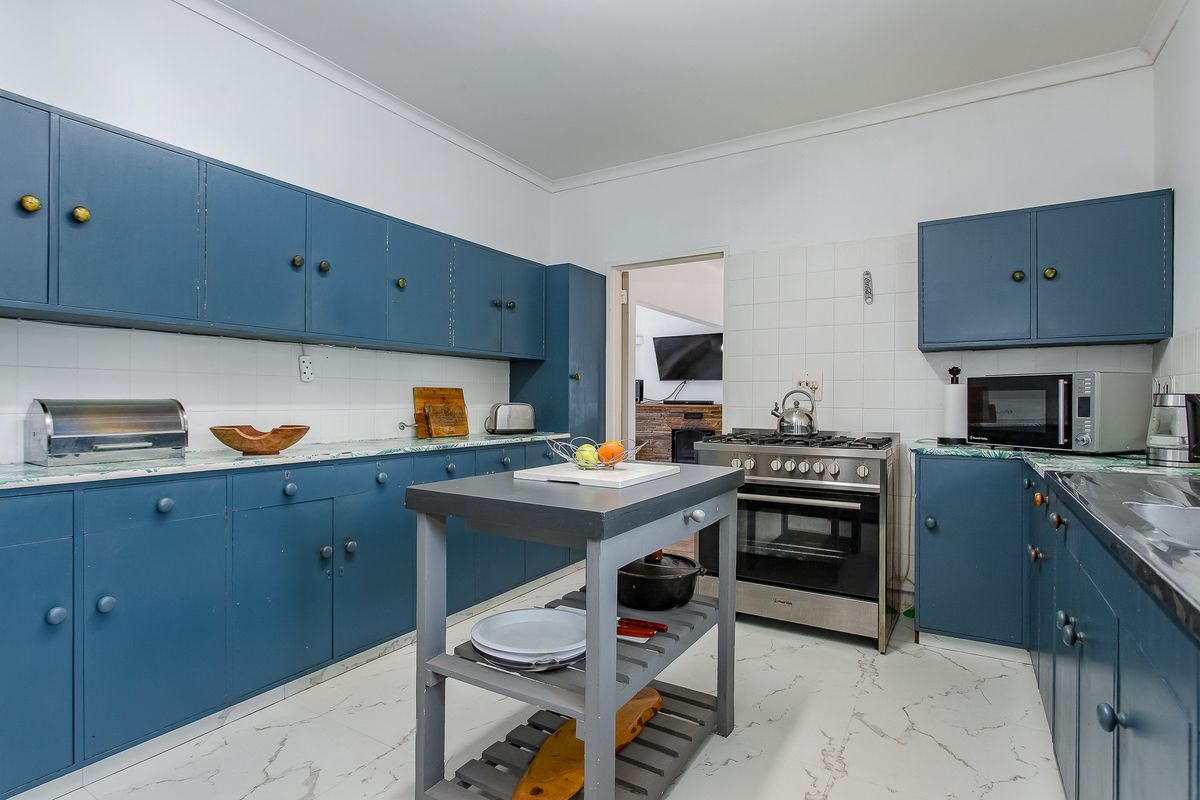 A functional kitchen featuring blue built-in cabinetry, a gas stove with oven, tiled backsplash, and marble-look countertops with a central prep island.