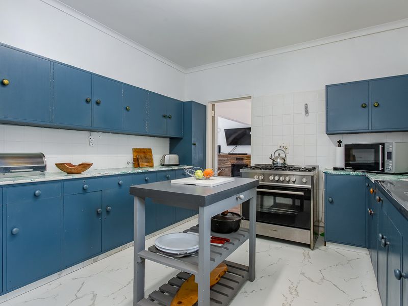 A functional kitchen featuring blue built-in cabinetry, a gas stove with oven, tiled backsplash, and marble-look countertops with a central prep island.