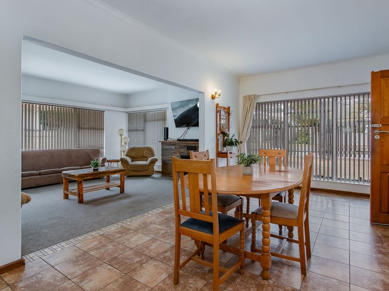 Open-plan living and dining area featuring tiled and carpeted flooring, a stone-clad fireplace, and large windows with vertical blinds.