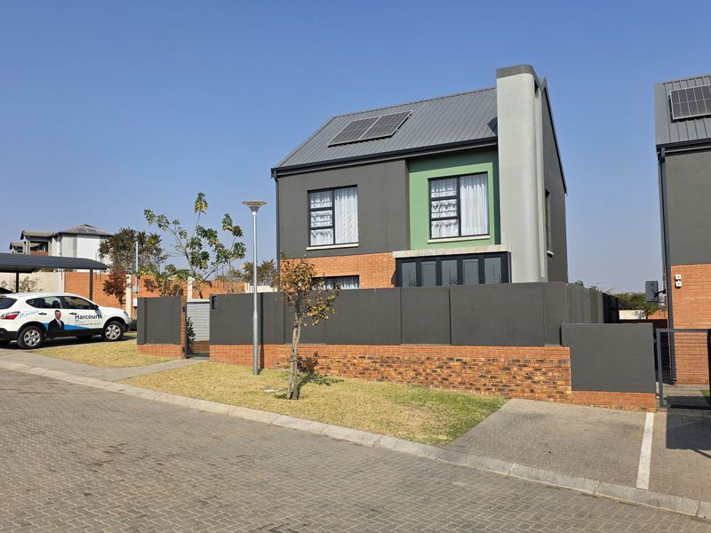 Front view of a modern two-story townhouse featuring a brick and rendered facade, metal roof with solar panels, and a private paved driveway with carport.