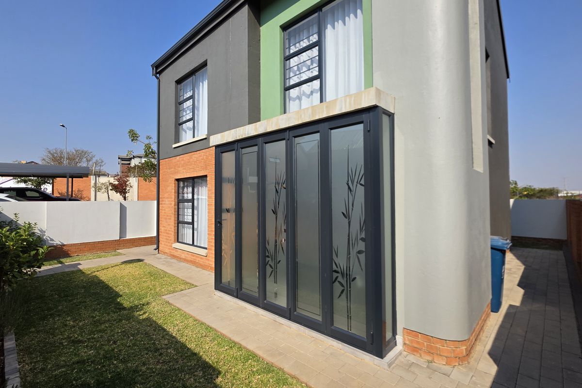 Rear view of a modern townhouse featuring bi-fold glass doors, brick and rendered facade, and a private garden area.